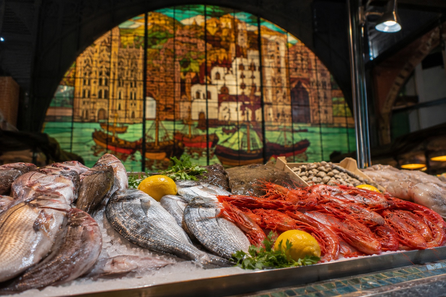 Fiskstånd i Atarazanas-marknaden i Málaga med färska havskräftor, hel fisk på is och citroner — glasmålningsfönster i bakgrunden
